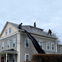 Three workers installing roofing on house